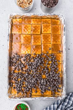 a cake with chocolate chips and caramel icing next to bowls of sprinkles