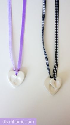 two necklaces with hearts hanging from them on a white surface, one has a purple ribbon and the other is black and white