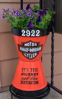 an orange motor cycle planter with purple flowers in it's center and the words, it's the journey to destination