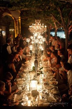 a long table with many people sitting at it and lit candles on the tables in front of them