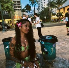 a woman sitting on the ground in front of trash cans with other people around her