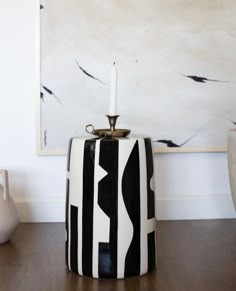 a black and white vase sitting on top of a wooden table next to a painting