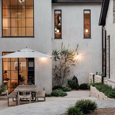 an outdoor dining area in front of a large white building with lots of windows and plants