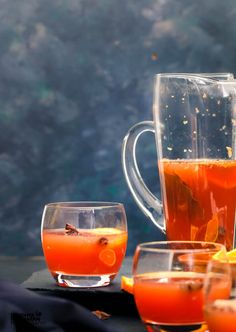 several glasses and pitchers filled with liquid sitting on a table next to an orange slice