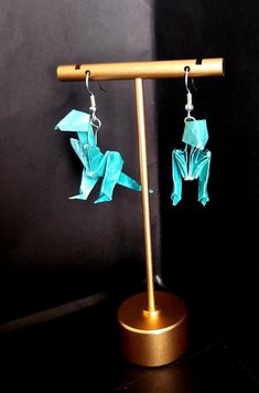 two origami birds are hanging from the earwires on a gold stand