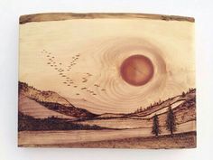 a wooden plaque with an image of birds flying in the sky over a mountain range