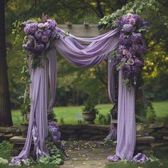 an outdoor wedding ceremony with purple flowers and draping on the arch, surrounded by greenery