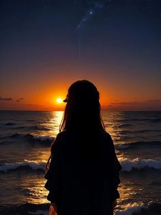 a woman standing on the beach watching the sun set over the ocean and stars in the sky