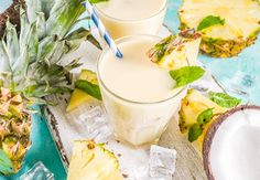 three glasses filled with pineapple milk next to sliced pineapples and ice cubes