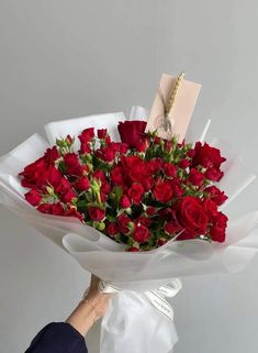 a person holding a bouquet of red roses in their hands with a note attached to it