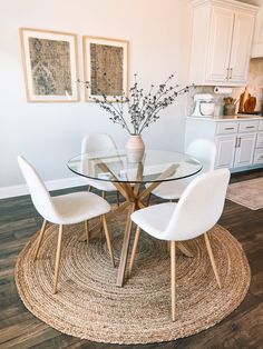 a glass table with four white chairs and a round rug in front of the table