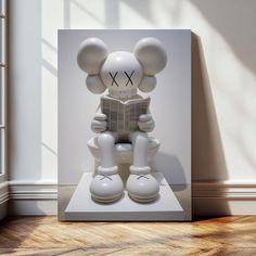 a sculpture of a mouse reading a book on top of a white pedestal in front of a window