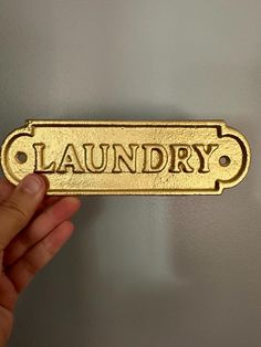 a hand holding up a gold sign that says laundry on the side of a wall