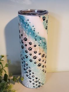 a blue and white tumbler with paw prints on it next to a plant in front of a wall