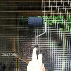 a hand is pointing at a bird in a cage that has mesh netting on it