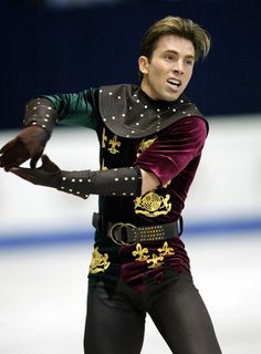 a male figure skating on an ice rink in a purple and black outfit with gold accents