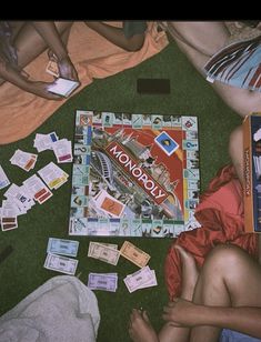 a monopoly board game laying on the ground with people around it and cards scattered about