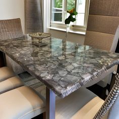 a marble dining table with matching chairs in front of a window and potted plant