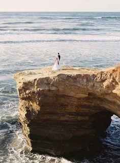 the bride and groom are standing at the edge of a cliff