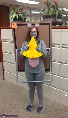 a woman dressed as a mouse holding a piece of cheese in front of her face