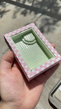 a hand holding a small green and pink box