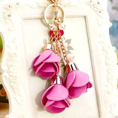 two pink flowers are hanging from a gold chain on a white frame with a flower keychain attached to it