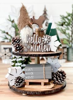 three tiered tray with christmas decorations and pine cones on it, along with the words hello winter