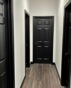 an empty hallway with black doors and wood flooring is pictured in this image from the front door