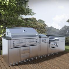 an outdoor kitchen with stainless steel cabinets and grills on the deck in front of trees