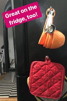 a red purse hanging from the side of a black refrigerator with magnets on it