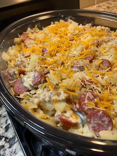 a casserole dish with sausage, cheese and potatoes in it on the stove