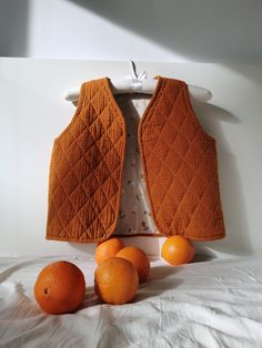 three oranges sitting on top of a bed next to an orange quilted vest