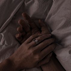 two hands holding each other while laying in bed