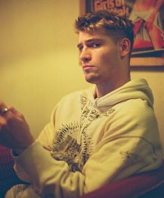 a young man sitting in a chair holding a remote control to his left hand and looking off into the distance