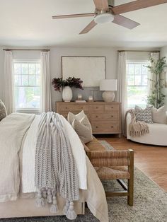 a bedroom with a large bed and two chairs in front of the window, along with a ceiling fan