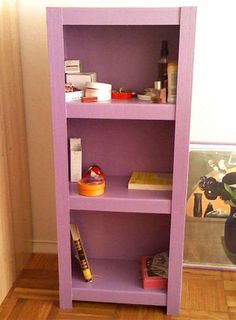 a purple book shelf sitting on top of a hard wood floor next to a vase