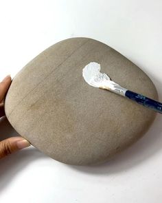 a person is holding a paintbrush in their left hand near a rock that has been placed on it