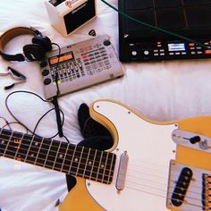 an electric guitar, headphones and other musical equipment on a bed with white sheets