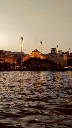 a body of water with buildings in the background at sunset or dawn, and lights reflecting on the water