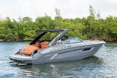 a gray boat with an orange seat is in the water near some trees and bushes