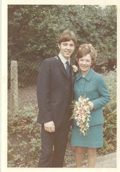 an old photo of two people standing next to each other in front of some trees