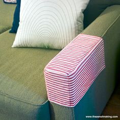 a green couch with red and white striped pillow on it's armrests