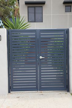 a large blue gate in front of a white building with palm trees and bushes behind it