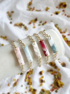 four necklaces with different colored stones hanging from gold chains on a white fabric background