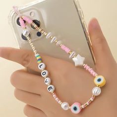 a hand holding a cell phone with an eye charm on it's wrist and bracelet