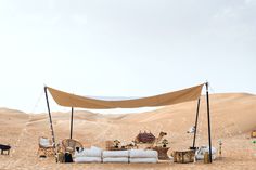 an outdoor tent set up in the desert with chairs and tables under it, surrounded by sand dunes