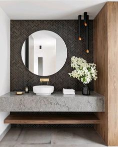 a bathroom with marble counter tops and a round mirror on the wall, along with a vase filled with flowers