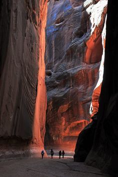 three people are walking through a narrow canyon