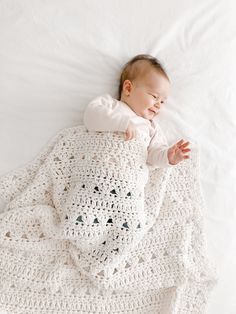 a baby laying on top of a bed covered in a white crochet blanket