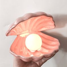 a hand holding a pink shell shaped object with a white ball in it's center